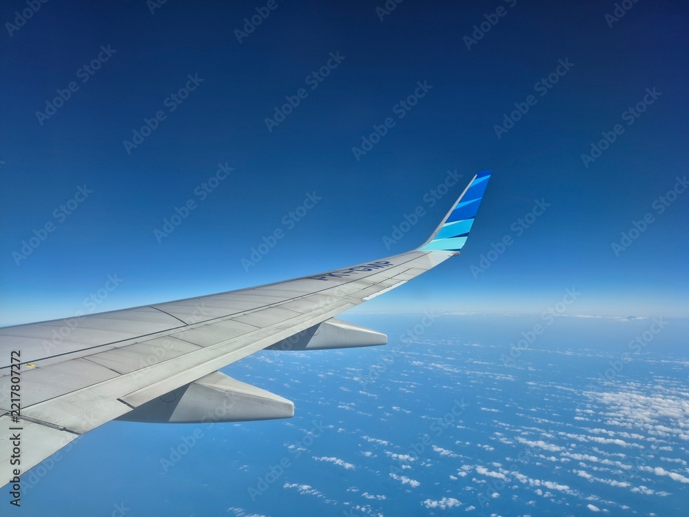 Fototapeta premium Airplane wing flying high in the clear blue sky over clouds during a sunny flight