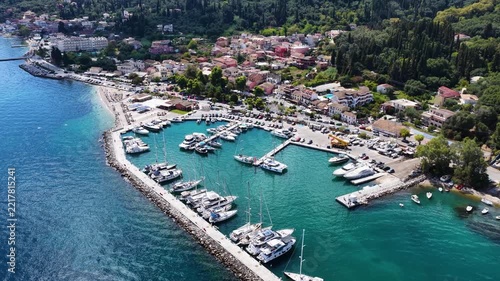 Aerial drone view of Benitses marina and harbor in Corfu, Greece. Yachts and boats docked in clear blue Ionian sea by the coastal town