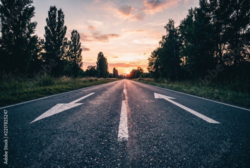 Asphalt road with white painted direction arrows pointing left right and straight forward at sunset, strategic decision making, business choices, future opportunity path