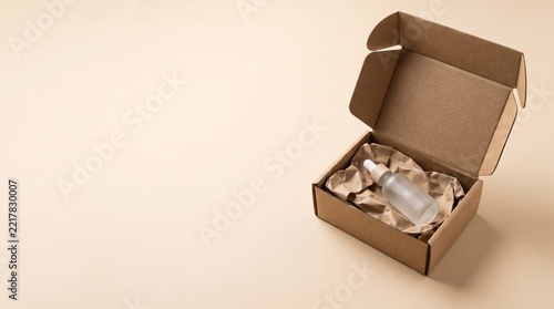 Open cardboard mailer box containing a cosmetic dropper bottle surrounded by eco-friendly paper packaging on a beige background