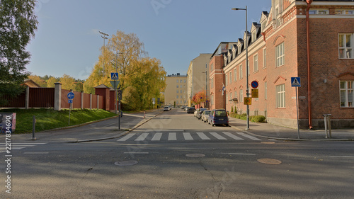 Sunny autumn street scene with historic red brick architecture, trees, parked cars and a pedestrian crossing in Tampere, Finland.