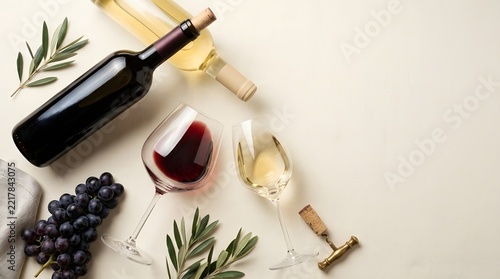An elegant still life featuring two wine bottles  two filled wine glasses  a cluster of dark grapes  and olive branches on a textured fabric background