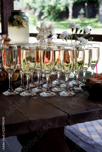 multiple champagne flutes with sparkling wine lined up on a dark wooden table
