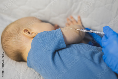 Doctor giving vaccine injection into an infant's arm with a syringe during routine medical procedure.