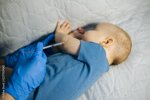Pediatrician in blue gloves giving a vaccine injection into a baby's arm during routine healthcare vaccination.