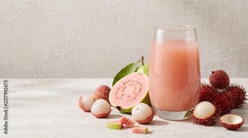 Glass of Fresh Pink Guava and Lychee Juice with Tropical Fruits on Stone Table