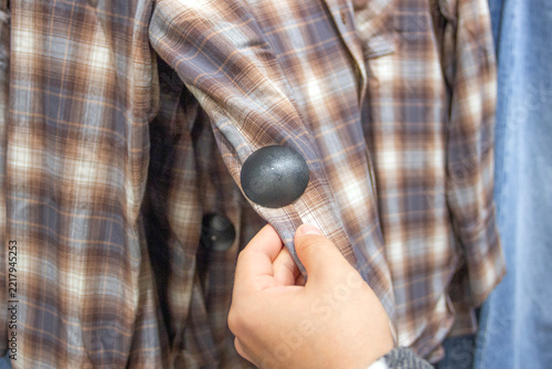 hand holding a shirt with a security bag on it, choosing clothes in a shop, anti-theft security tag