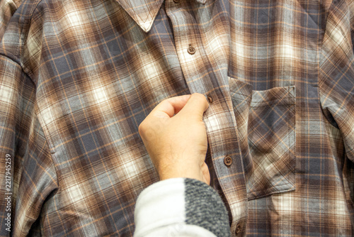 man buttoning a checkered shirt, choosing new clothes in a clothes store