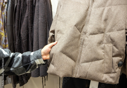 hand holding a winter coat, choosing a warm coat for winter 2027, clothes shop