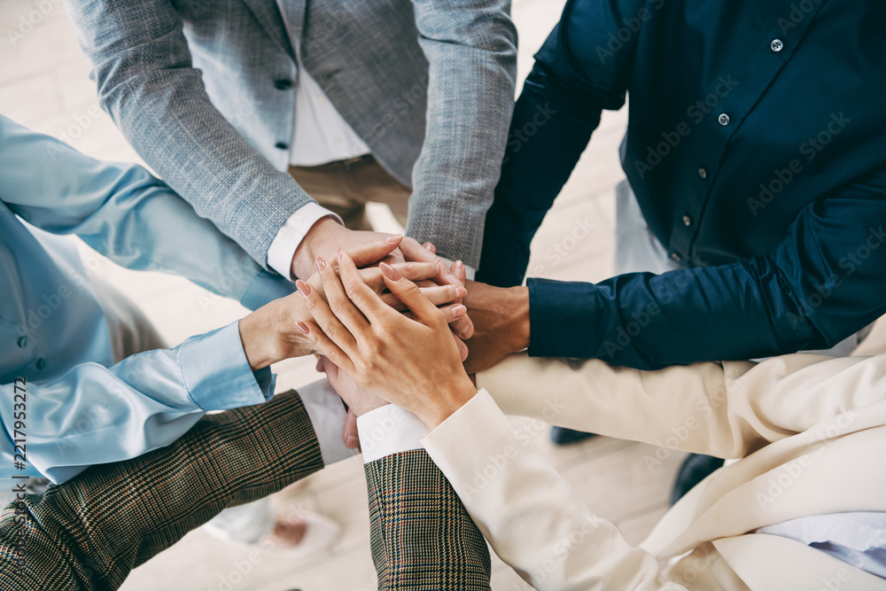 Obraz premium Professional colleagues stacking hands in a meeting, showcasing teamwork and collaboration in a formal business office environment