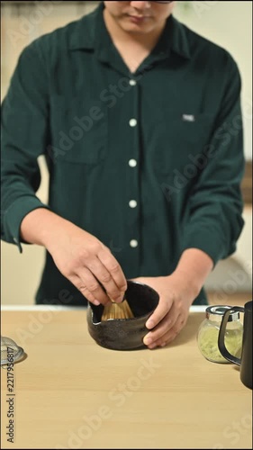 Closeup Hands whisking matcha powder in ceramic bowl on kitchen counter