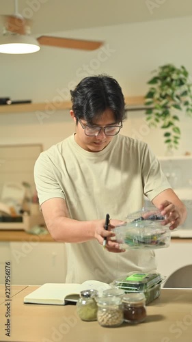 Asian Man Writing Nutrition Checklist with Fresh Groceries in Kitchen