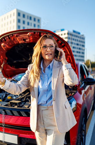 Stressed business woman calling roadside assistance near broken car.