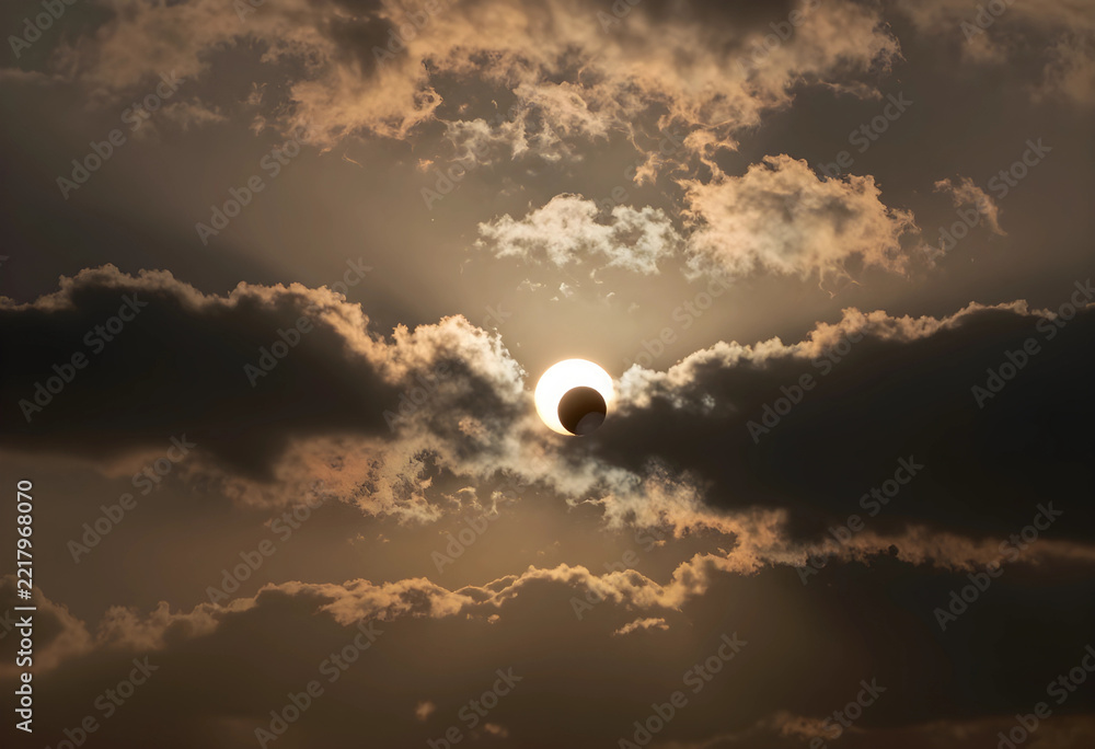 Fototapeta premium Solar eclipse and astronomy event, partial sun obscuration by moon with dramatic clouds and light rays in the sky during a rare celestial phenomenon