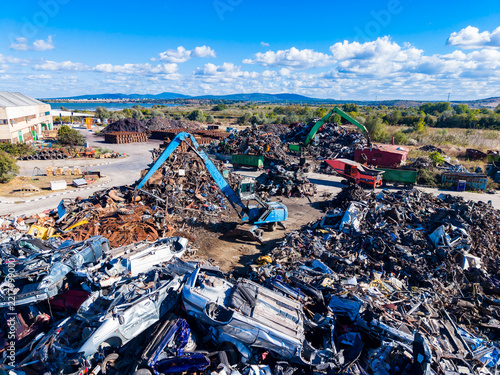 Scrapyard with multiple cars and machinery under a clear blue sky