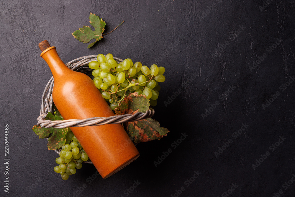 Naklejka premium Terracotta wine bottle and green grapes in a wicker basket