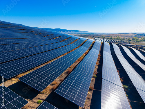 Solar panels are installed on a hillside under a clear blue sky, capturing sunlight in a renewable energy farm