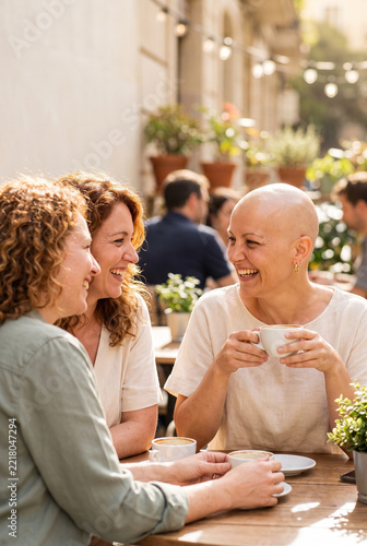 Three women laughing and talking over coffee at an outdoor café  