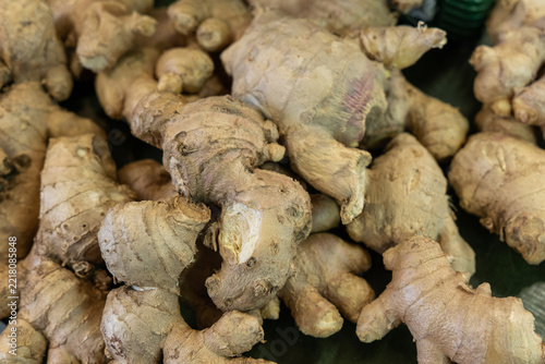 Close-up pile of fresh ginger root rhizomes with papery beige-brown skin, knobby irregular shapes on dark background textural macro detail for food ingredient display