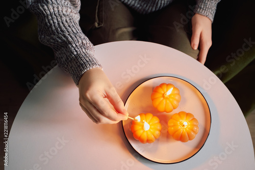 Top view of woman lighting pumpkin candles on plate for cozy home autumn decor