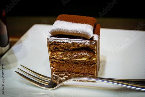 Popular Japanese fusion chocolate mousse and sponge black forest cake dessert sprinkled with icing sugar and served on a white plate with a fork in Osaka, Japan.