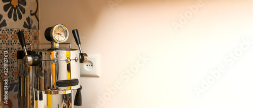 Shiny modern chrome espresso machine standing on a kitchen counter against a light wall. Coffee making and appliance concept. Banner with copy space