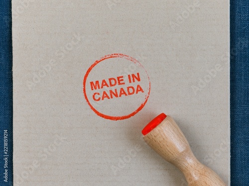 Made in Canada stamp impression on grainy beige cardboard with a wooden handle, featuring a rustic orange ink mark for export and origin labels