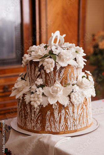 Traditional Ukrainian wedding cake decorated with white sugar flowers wheat patterns on wooden surface indoors