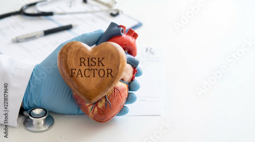 Doctors Gloved Hand Holding Anatomical Heart Model with Wooden Risk Factor Heart