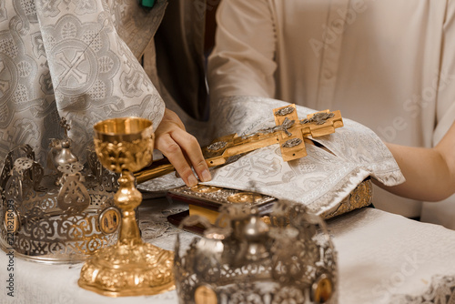 Fotografie Close up of priest's hand placing golden cross in church with chalices crowns ve