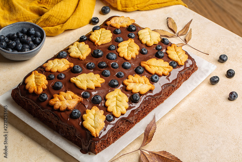 Closeup of Homemade rectangular chocolate sheet cake covered with rich chocolate ganache and decorated with yellow oak leaf cookies and fresh blueberries. Autumn-inspired cake 