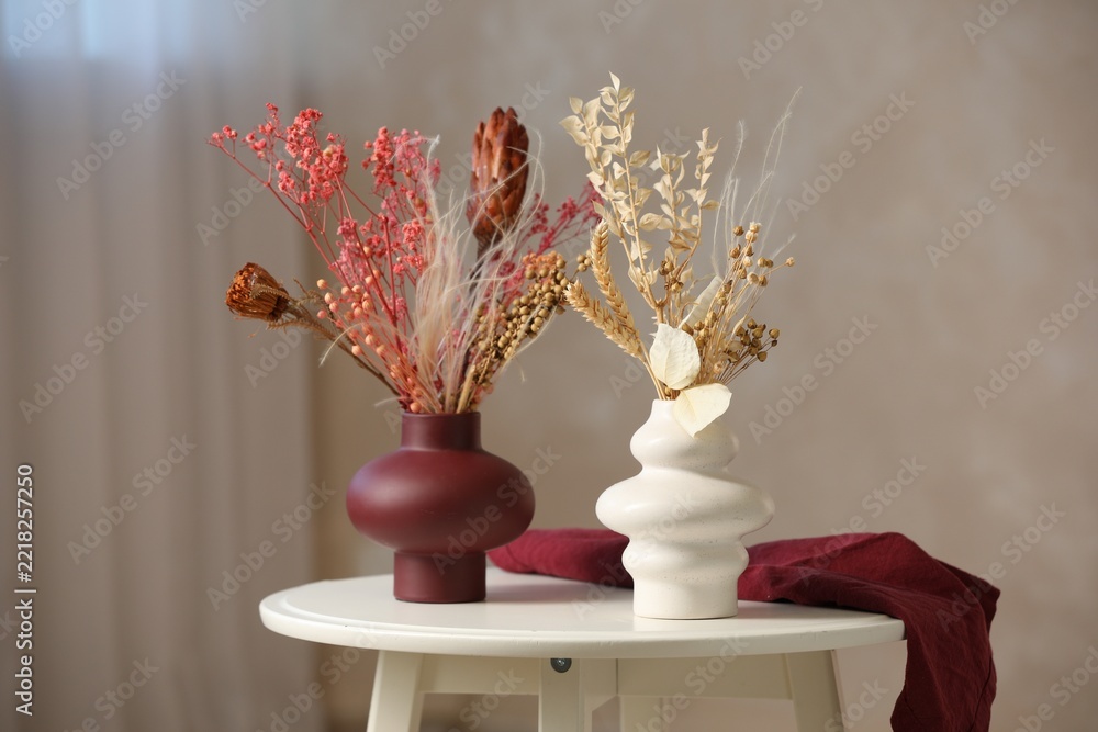 Naklejka premium Beautiful dried plants in vases on table against beige background