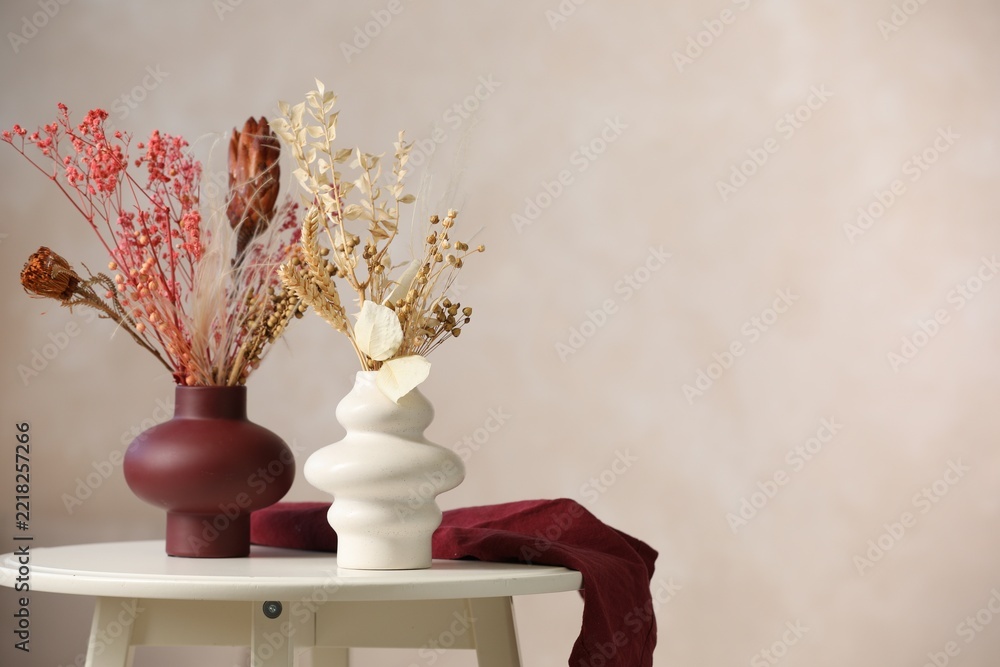 Fototapeta premium Beautiful dried plants in vases on table against beige background. Space for text