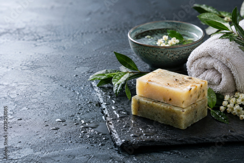 Handcrafted soap bars with rolled towel and greenery on wet dark stone