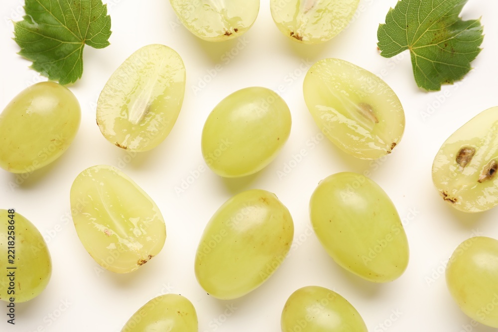 Fototapeta premium Fresh ripe grapes and green leaves on white background, flat lay