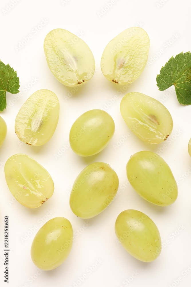 Fototapeta premium Fresh ripe grapes and green leaves on white background, flat lay