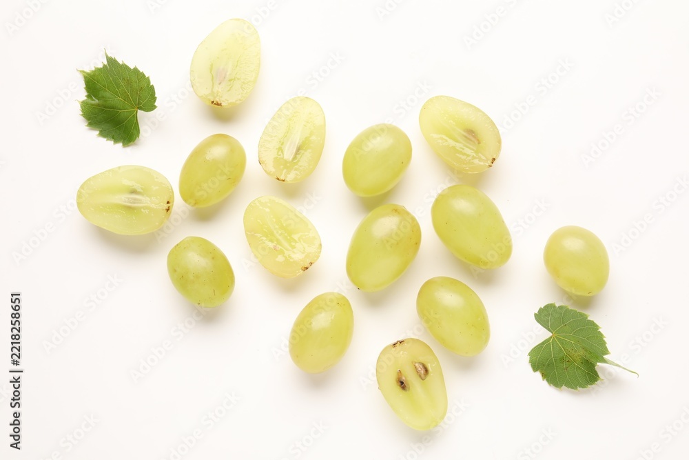 Fototapeta premium Fresh ripe grapes and green leaves on white background, flat lay