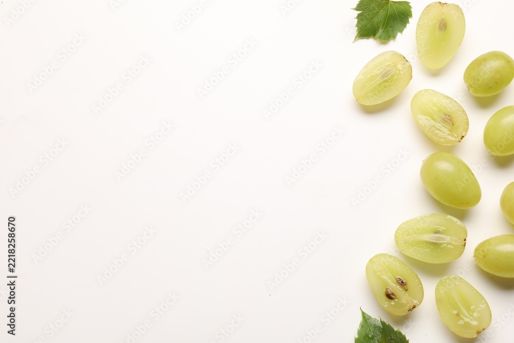 Fototapeta premium Fresh ripe grapes and green leaves on white background, flat lay. Space for text