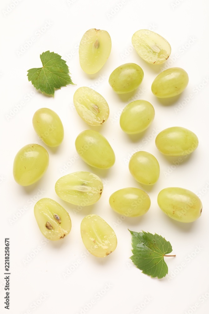 Fototapeta premium Fresh ripe grapes and green leaves on white background, flat lay