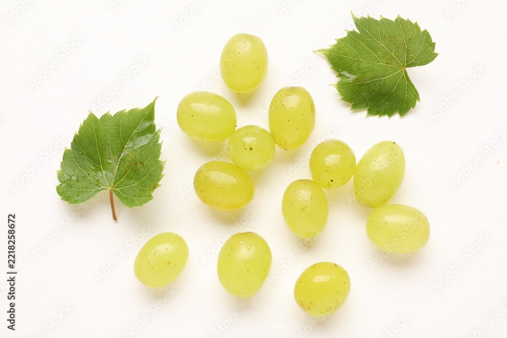 Fototapeta premium Fresh ripe grapes and green leaves on white background, flat lay