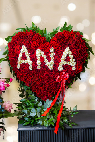 Beautiful heart shaped red rose flower arrangement with white roses spelling ANA word for Mothers Day gift in luxury room interior setup. Romantic floral decoration for celebration.