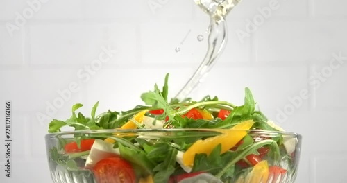 Sunflower oil pouring from bottle onto fresh vegetable salad with arugula tomato pepper and white cheese