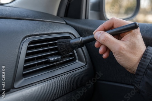 Car detailer cleaning a dashboard air vent with a soft brush