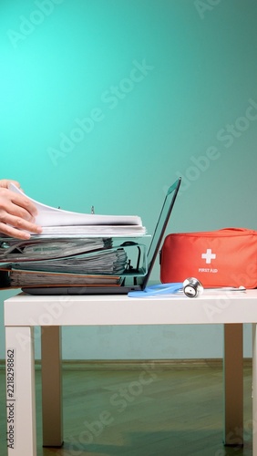 Healthcare professional managing patient records and hospital bureaucracy with a laptop, stethoscope, and first aid kit on a desk, highlighting busy medical administration