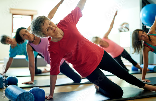 Active, senior and woman in pilates class for wellness, mobility exercise and healthy body. Side plank, elderly and female person in gym studio for workout, fitness training and physical wellbeing.