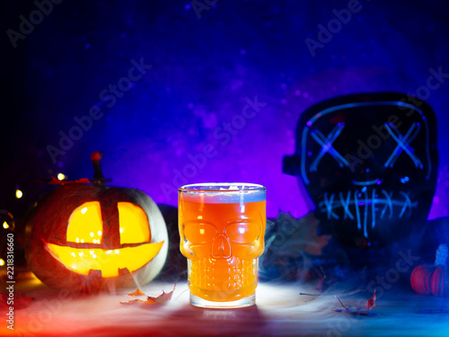 beer glass on the table with a pumpkin lantern and a spooky mask, celebrating Halloween. A skull glass with pumpkin beer.