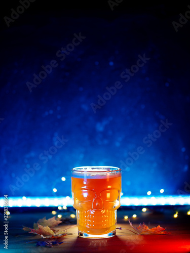 Halloween beer on the table with autumn leaves, blue lighting, and copy space.