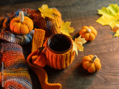 autumnal cozy scene. A mug of coffee on a wooden table. A knitted warm scarf and small orange pumpkins. Autumnal decoration.