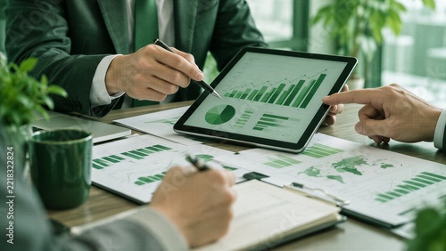 Business professionals analyzing financial data on digital tablet and papers during corporate meeting for strategy and planning.