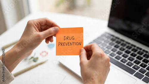 Drug prevention note held near laptop in office workspace, anti addiction concept with hands and desk, photorealistic commercial stock image